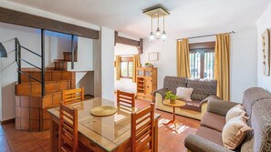 A modern living room with a sofa, a dining table with chairs, a staircase, and a kitchen area.