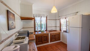 Eine kleine Küche mit weißen Fliesen, einer Holz Arbeitsplatte, einem eingebauten Backofen, einem Spülbecken und einem Kühlschrank.