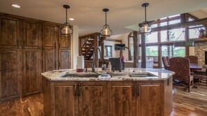 Een ruime keuken met houten kastjes, een groot eiland met een spoelbak en hangende lampen.