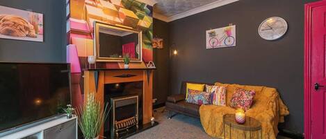 A living room with a fireplace, a sofa, a television, and a red door.