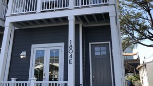 Un edificio de varios pisos con fachada oscura y detalles blancos, que cuenta con balcones y una puerta principal con una placa numérica.