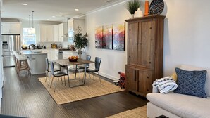 Una cocina moderna con armarios blancos, un comedor con mesa y sillas de madera, y una sala de estar con sofá y un aparador decorativo.