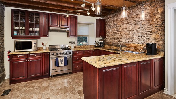 A kitchen with dark wood cabinets, a granite countertop, a stone wall, and hanging pendant lights. - Arrowstone Luxury Farmhouse in Historic Old Town, Niagara-on-the-Lake.  (Niagara-on-the-Lake)