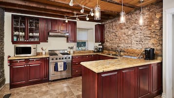 Eine Küche mit dunklen Holzausbau, einer Granit Arbeitsplatte, einem eingebauten Backofen, einer Mikrowelle und einer Steinwand.