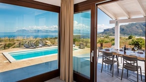 Una villa moderna con balcón de cristal que da a una piscina y una vista panorámica del océano.