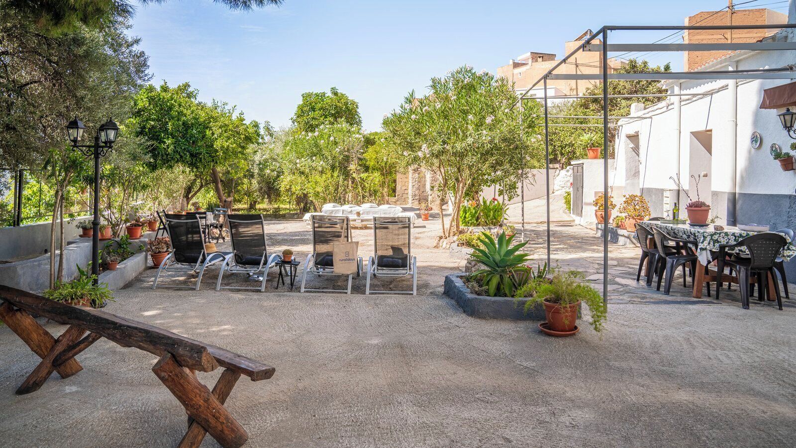 Un espace extérieur aménagé en patio, avec des coins salon, des plantes en pot et un banc en bois rustique.