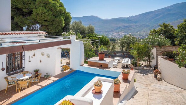 A rooftop pool with a view of mountains, surrounded by potted plants and outdoor furniture. - Huerta La Niña Arenas Órgiva by Ruralidays (Granada)