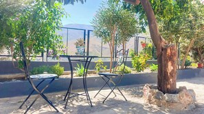 An outdoor seating area with a table and chairs, surrounded by greenery and a fence. - Huerta La Niña Arenas Órgiva by Ruralidays (Granada)