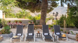 Outdoor seating with lounge chairs and a table, surrounded by potted plants and a mountainous backdrop. - Huerta La Niña Arenas Órgiva by Ruralidays (Granada)