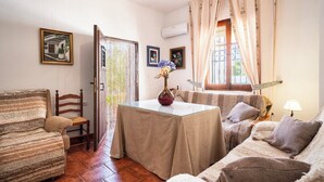 A cozy living room with a sofa, a dining table with a vase, and a chair. - Huerta La Niña Arenas Órgiva by Ruralidays (Granada)