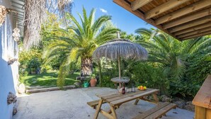 A wooden table with a thatched umbrella, a bottle, and glasses, surrounded by lush greenery and palm trees. - Casa de La  Cascada Iznájar by Ruralidays (Córdoba)