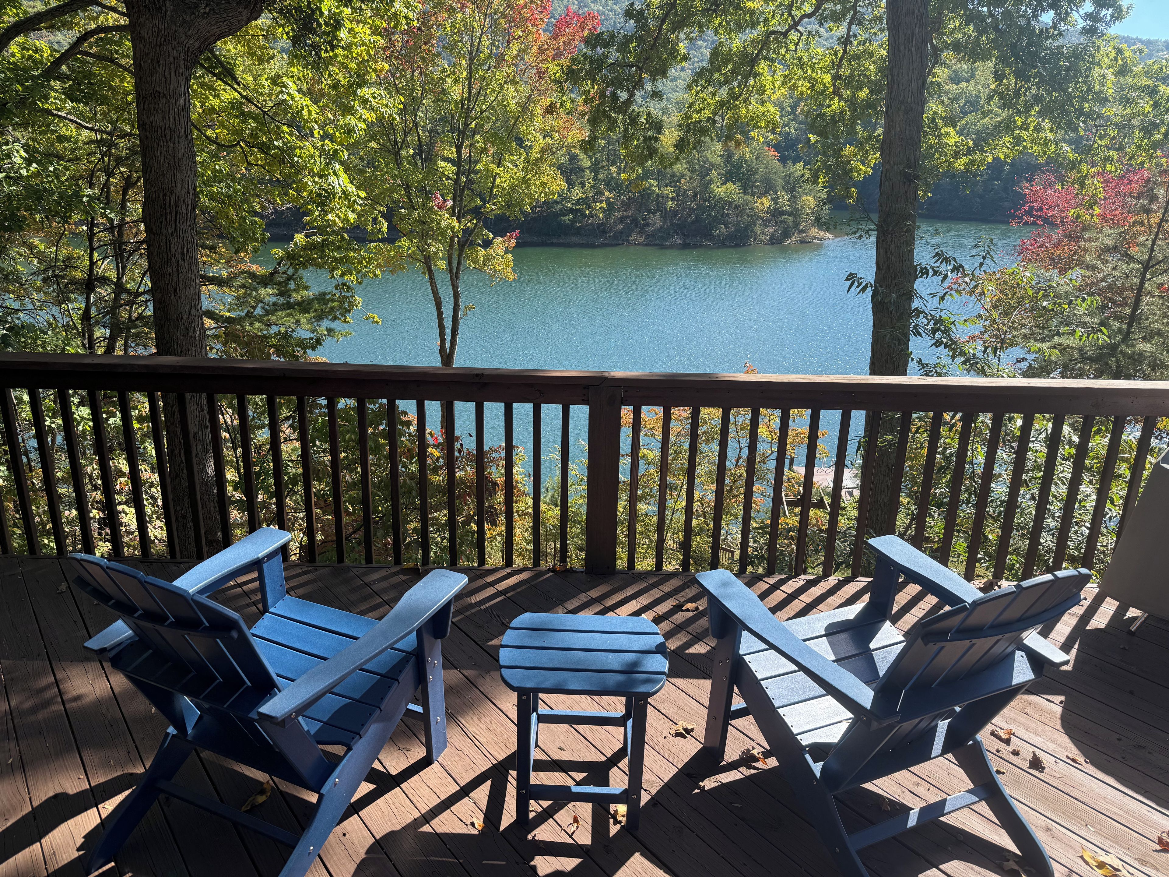 A wooden deck with Adirondack chairs overlooking a lake surrounded by trees.
