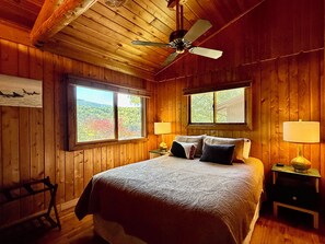 Habitación con paneles de madera, una cama, dos ventanas, un ventilador de techo y lámparas de noche.