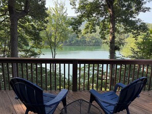 A wooden deck with two blue chairs facing a lake surrounded by trees.