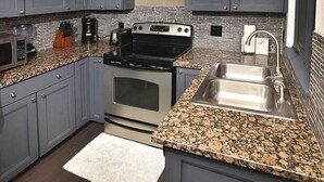 Una cucina moderna con mobili grigi, lavello in acciaio inossidabile, piani in granito, forno a incasso e cappa aspirante.