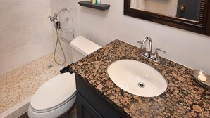Un bagno con un WC bianco, un lavandino in granito, una doccia e uno specchio con porta asciugamani.