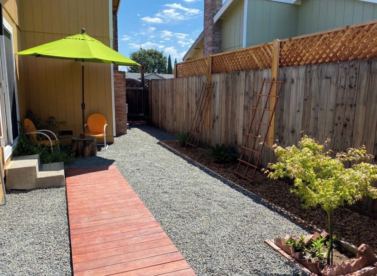 Uma área de pátio com deck de madeira, um guarda-sol verde e uma pequena árvore.