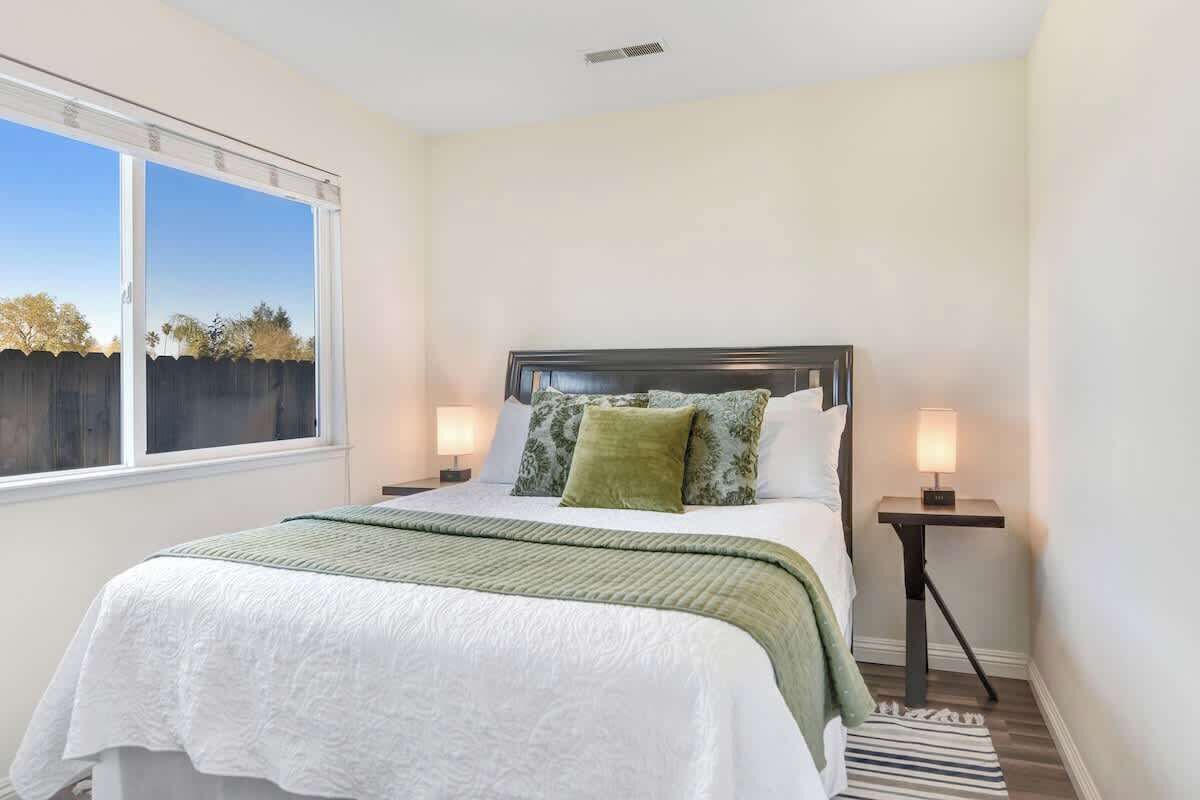 A bedroom with a bed, two bedside tables, a window, and a view of trees.