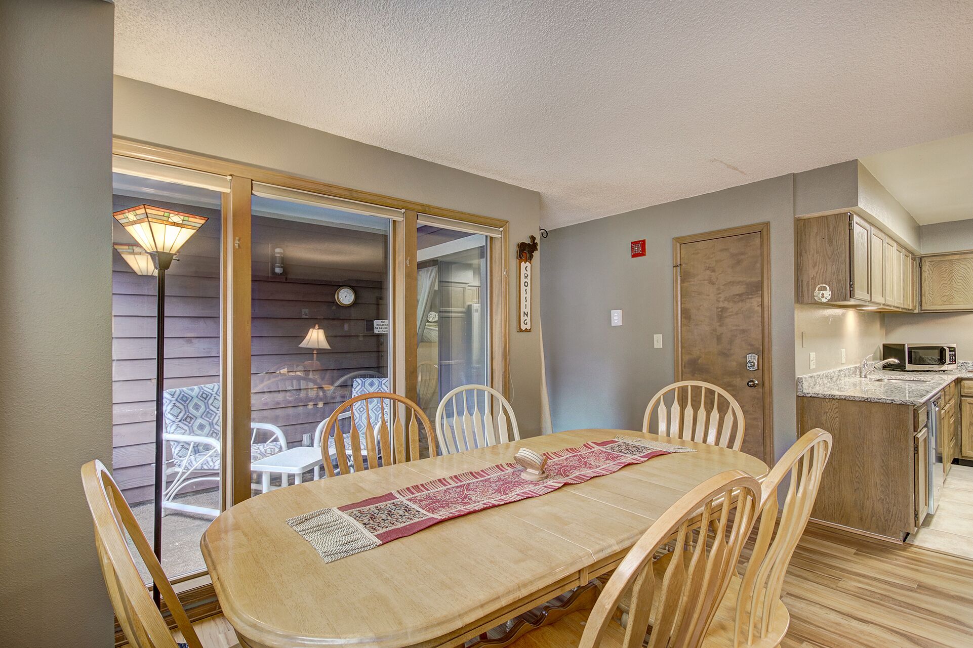 A dining area with a wooden table and chairs, a sliding glass door leading to a patio, and a kitchen with wooden cabinets.