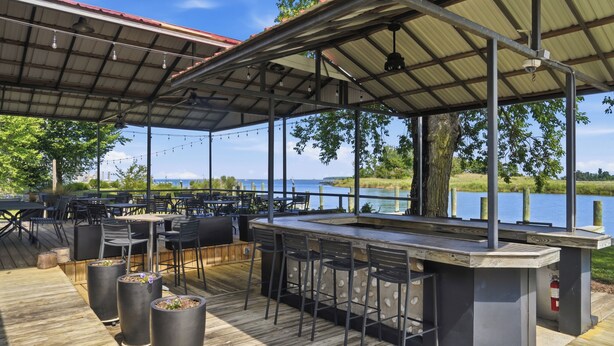 Ulkoterassi, jossa on baarialue, näkymä järvelle, puinen kansi ja metallinen kattorakenne.