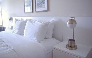 A neatly made bed with white linens and pillows, a bedside table with a lamp, and two framed pictures on the wall. - The Tilghman Island Inn (Tilghman)