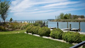 A grassy area with a wooden dock extending into a calm body of water, surrounded by greenery and a clear sky. - The Tilghman Island Inn (Tilghman)