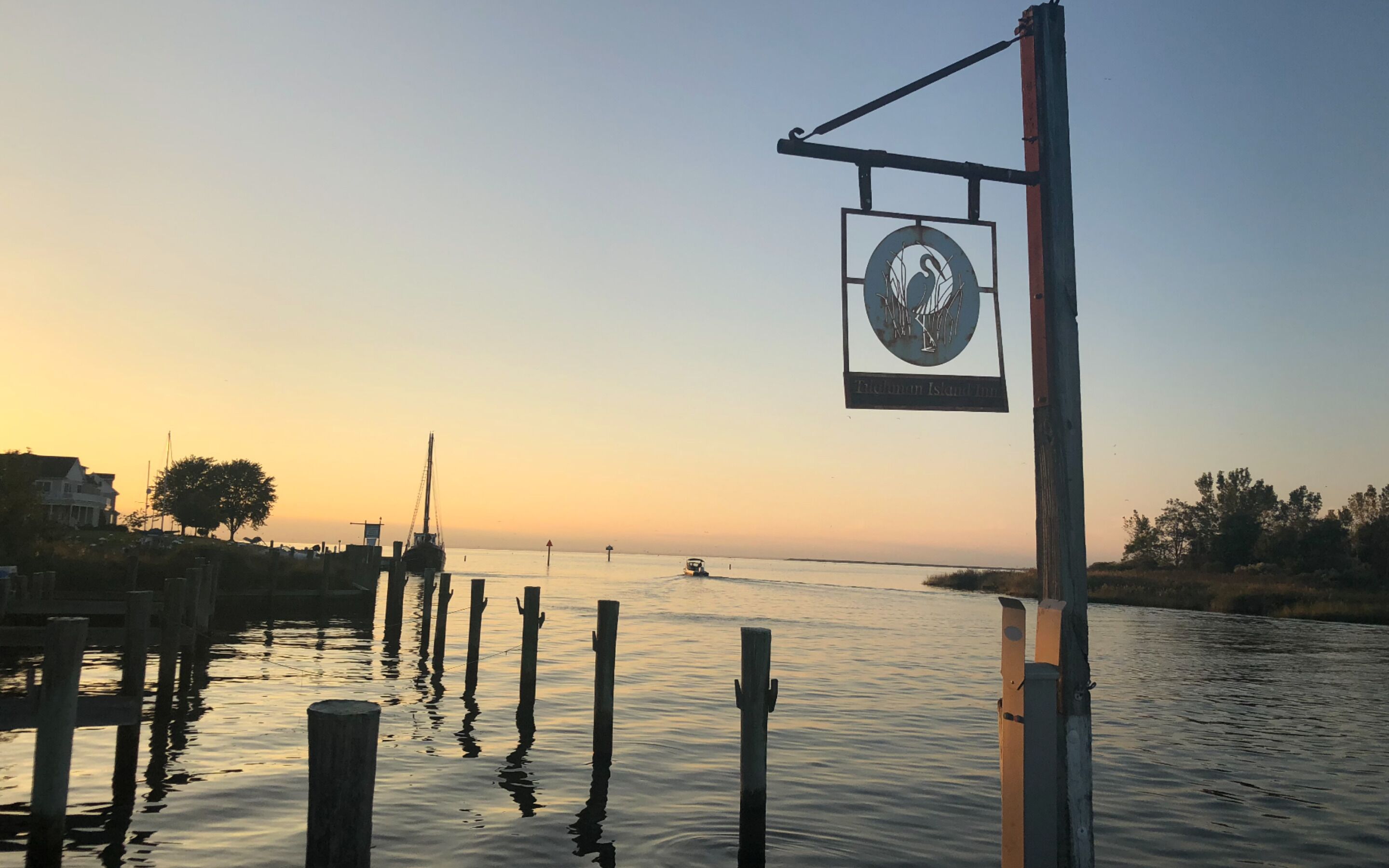 A waterfront scene with a signboard, wooden posts, and calm water reflecting the sky.