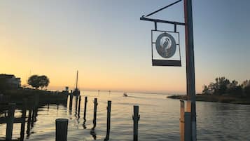 A waterfront scene with a signboard, wooden posts, and calm water reflecting the sky.
