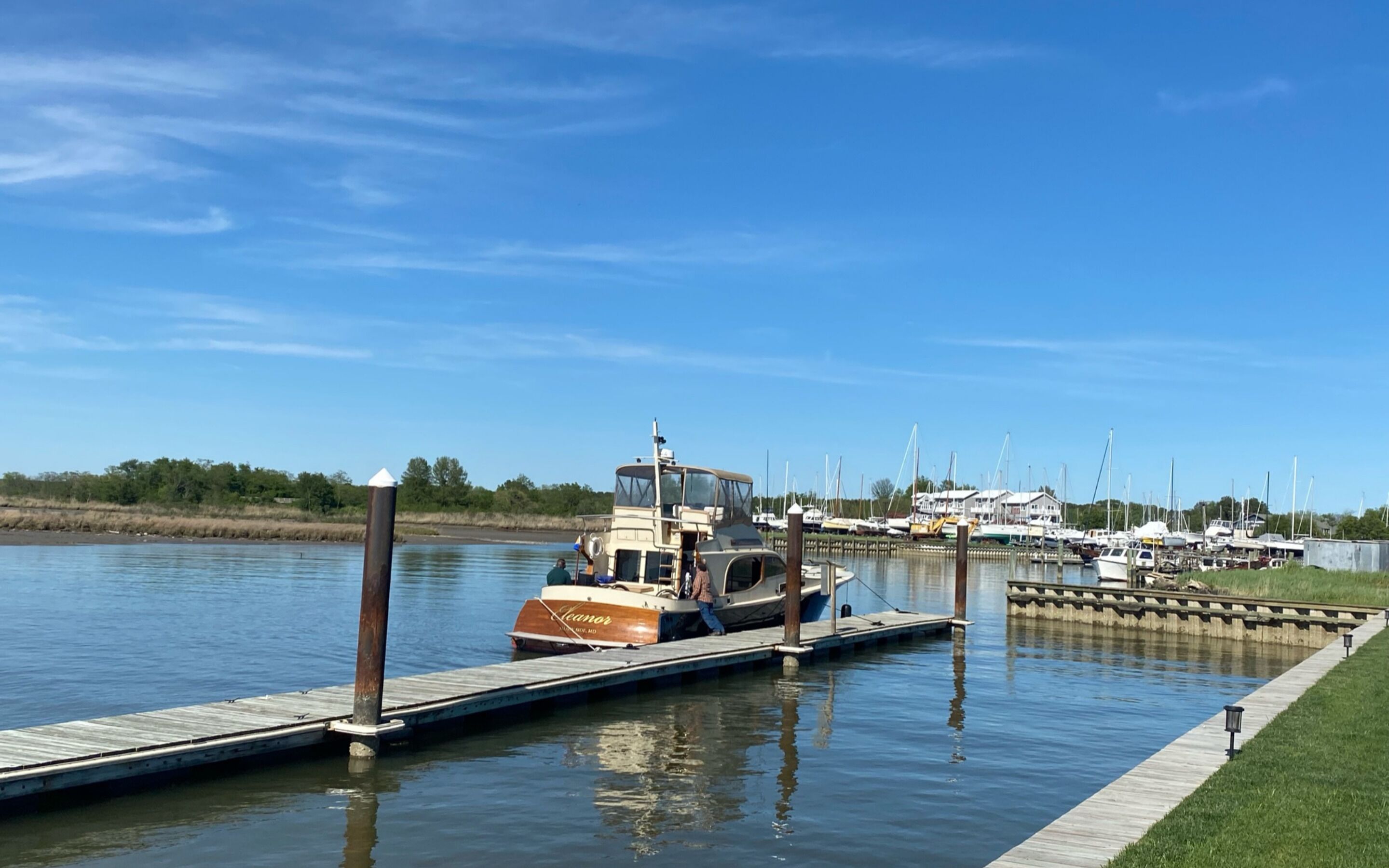 Un port de plaisance avec des bateaux amarrés, une jetée en bois et un ciel bleu azur.