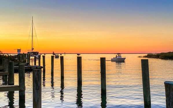 A calm waterfront at sunset with boats docked at wooden piers and a sailboat in the distance. - The Tilghman Island Inn (Tilghman)