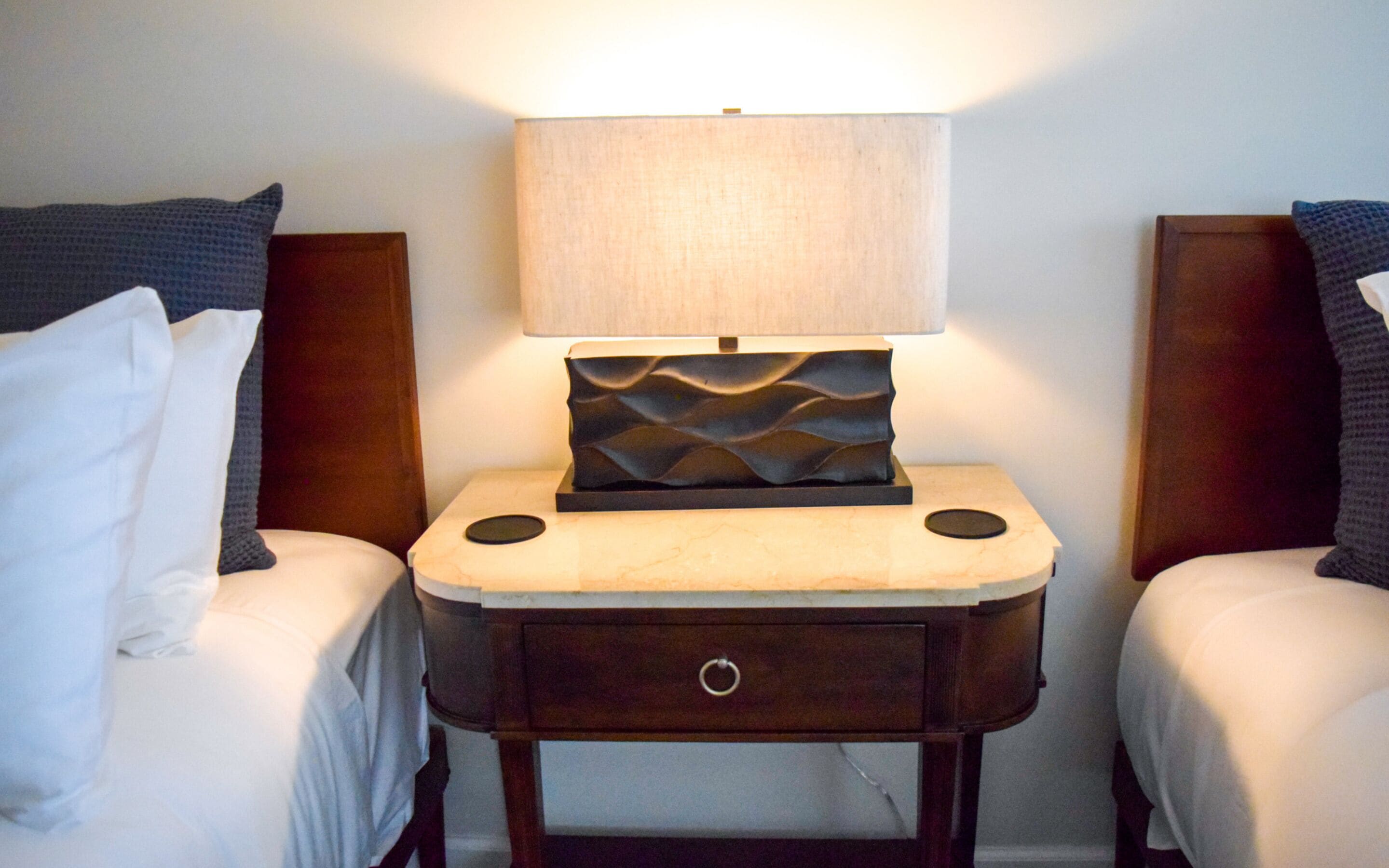 Een hotelkamer met twee bedden, een nachtkastje met een lamp en een klein lade.