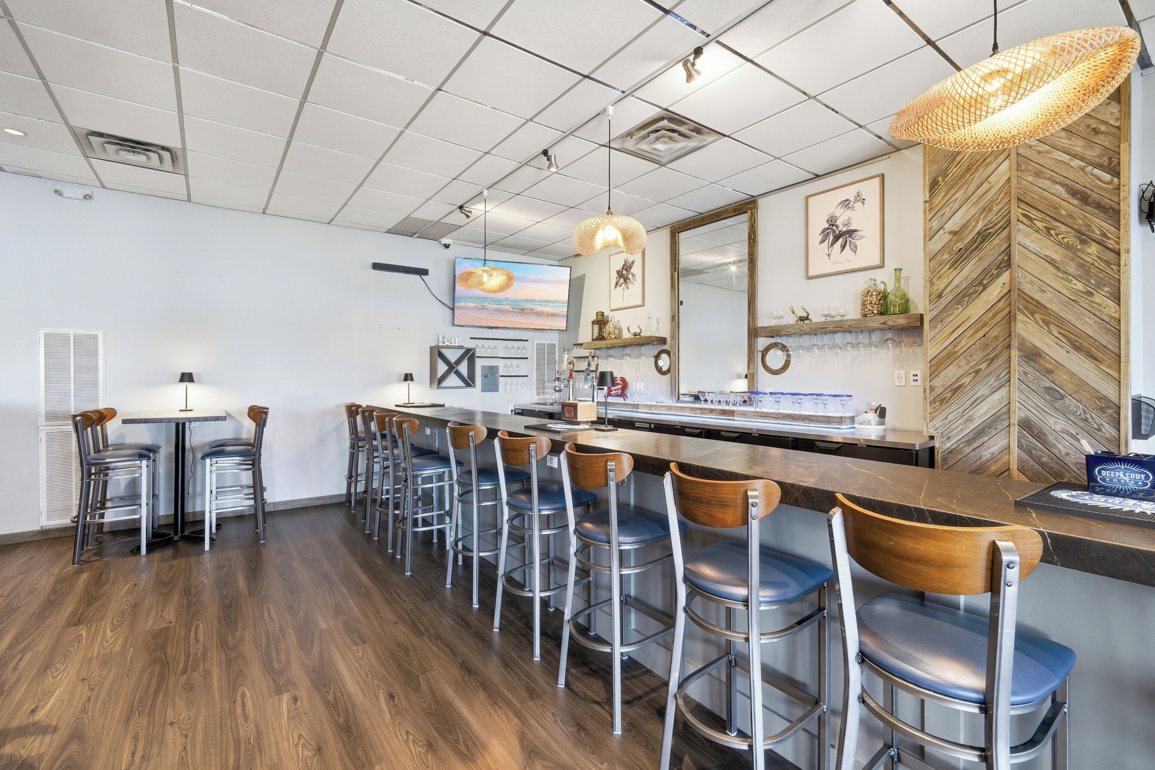 Un área de bar moderna con una barra larga, varios taburetes y un espejo grande.