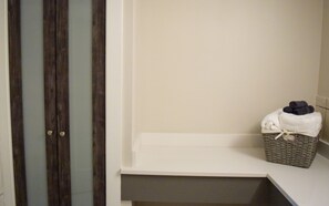 A bathroom with a wooden door, a white shelf, and a wicker basket with towels. - The Tilghman Island Inn (Tilghman)