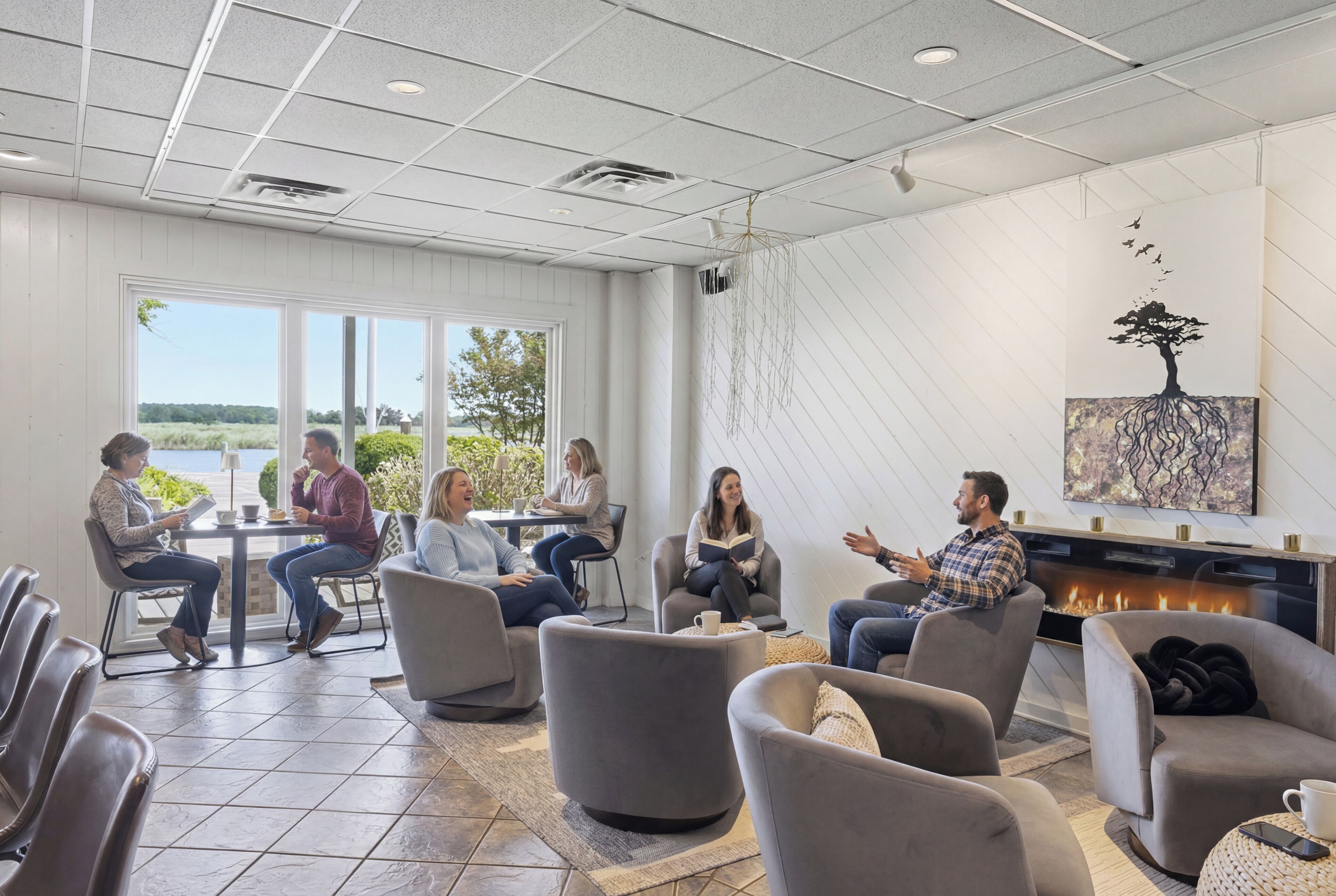 A modern lounge area with comfortable seating, a fireplace, and large windows offering a view of the outdoors.