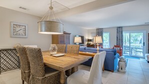 Un vaste espace de vie comprenant une table à manger en bois, des chaises à motifs, un canapé bleu et une grande fenêtre agrémentée de rideaux.