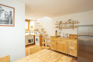 Une cuisine compacte équipée d’un four, d’un micro-ondes et d’un lave-linge intégrés, de meubles de rangement en bois et d’un réfrigérateur en acier inoxydable.
