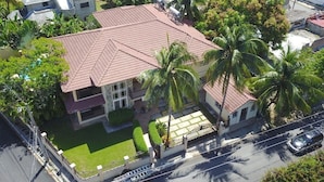 A two-story house with a red-tiled roof, surrounded by palm trees and a well-maintained lawn. - Luxurious Kickback Villa for Vacation Fun (Sosúa)
