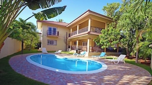 A two-story house with a swimming pool, surrounded by a brick patio and green lawn. - Luxurious Kickback Villa for Vacation Fun (Sosúa)