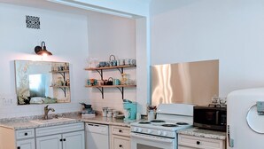 A modern kitchen with white cabinetry, a stove, microwave, and a sink. There are shelves above the counter holding various kitchen items.