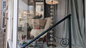 A cozy room with a white chair, a lamp, and a sign that reads "Be & Breakfast You Make Both."