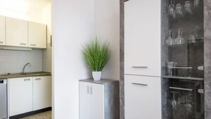 Une cuisine moderne avec des meubles blancs, un lave-vaisselle encastré, une plante en pot et un meuble vitré contenant de la verrerie.