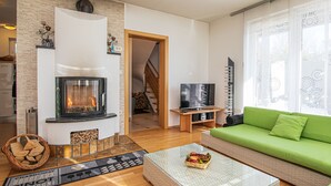 A modern living room with a fireplace, a green sofa, a glass coffee table, and a television.