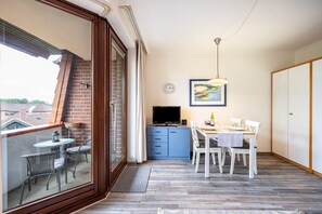 Balkon med udsigt, spiseplads med bord og stole, et fjernsyn og et ur på væggen.