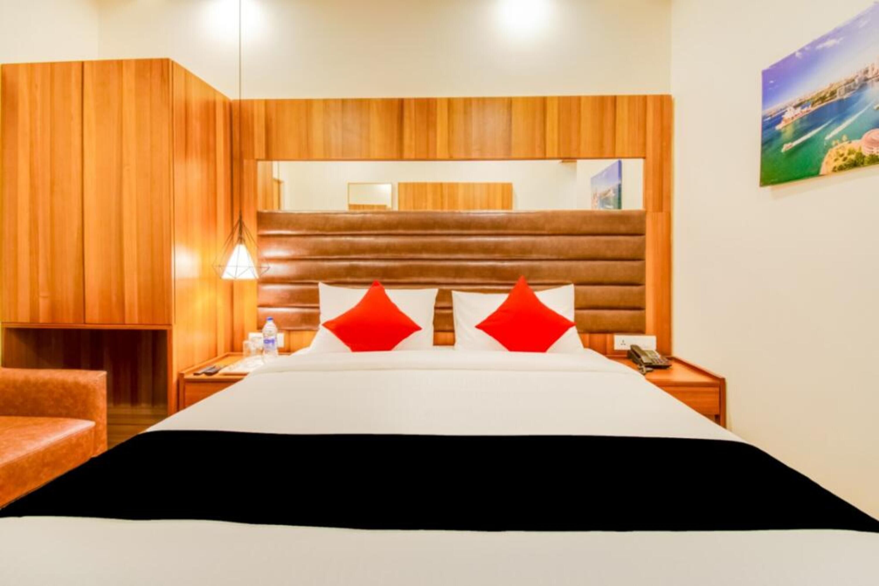Een hotelkamer met een houten hoofdeinde, een bed met witte en rode beddengoed, een nachtkastje met een lamp en een schilderij aan de muur.