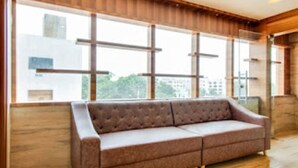 A modern room with a large window, a brown sofa, and wooden flooring. - Inn The Centre (Nellore)