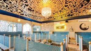 A mosque interior with blue seating, a chandelier, and a crescent moon symbol on the wall. - Inn The Centre (Nellore)