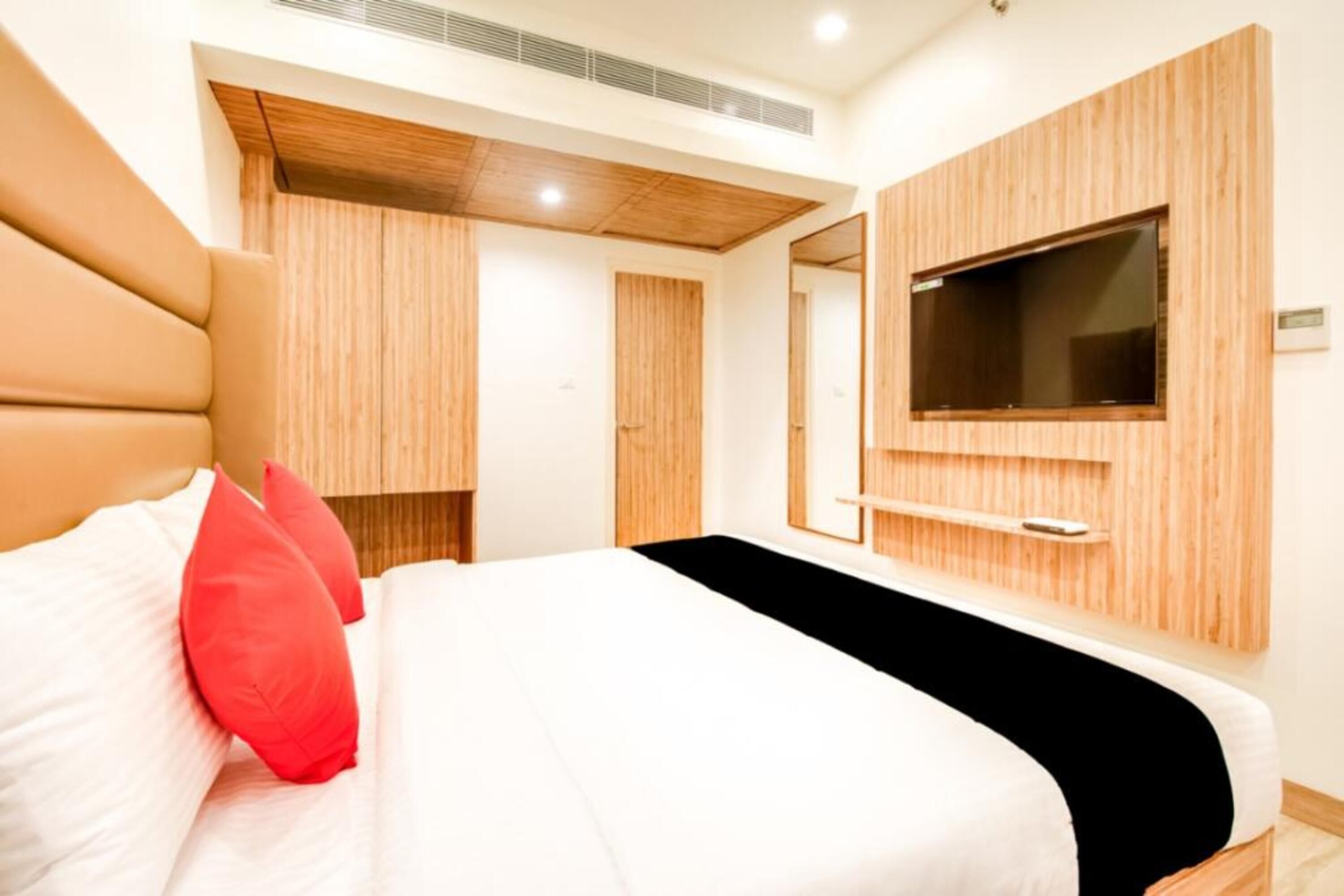 A modern hotel room with a large bed, wooden paneling, a TV mounted on the wall, and a small shelf.