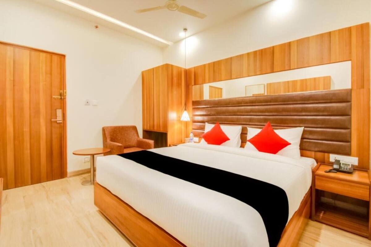 A hotel room with a large bed, wooden headboard, a small round table, a chair, and a bedside table with a phone.