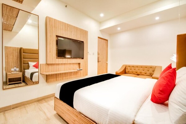 Una habitación de hotel moderna con una cama grande, un televisor montado en la pared, una mesita de noche y un armario.