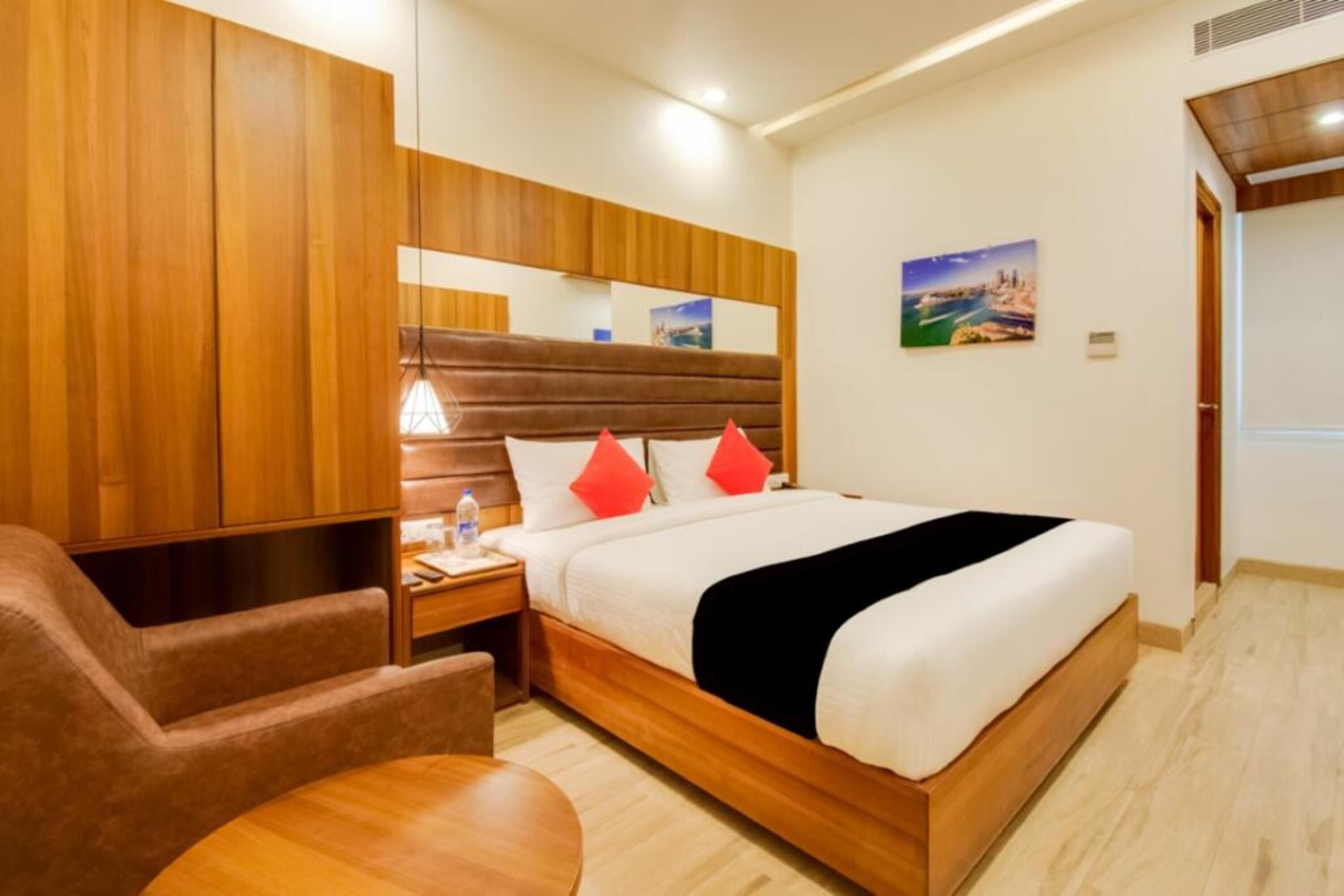 Una habitación de hotel con una cama de madera, una mesita de noche con lámpara, una silla y una pequeña mesa.